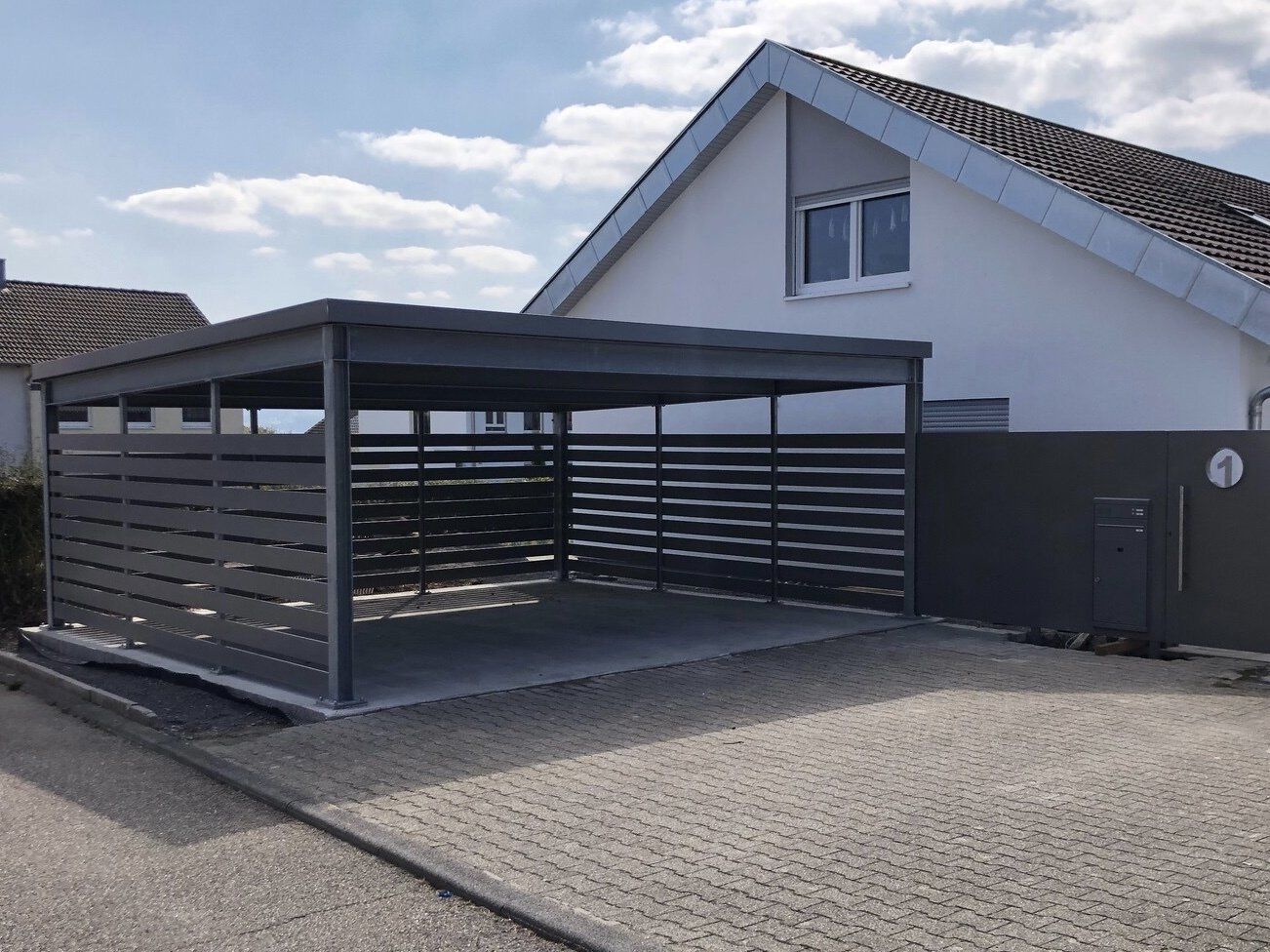 Vor einem weißen Haus steht ein Carport.