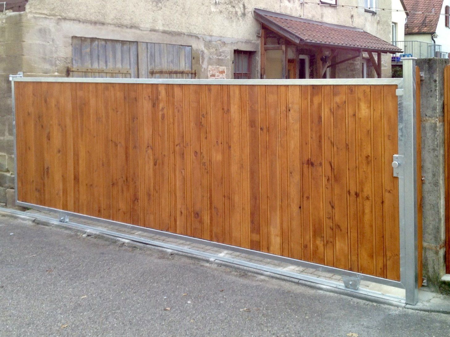 Ein Holzzaun mit einem Metallrahmen steht vor einem Gebäude