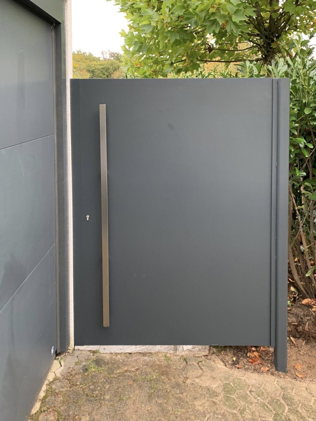 Neben einem Garagentor steht ein schwarzes Tor mit einem Edelstahlgriff.