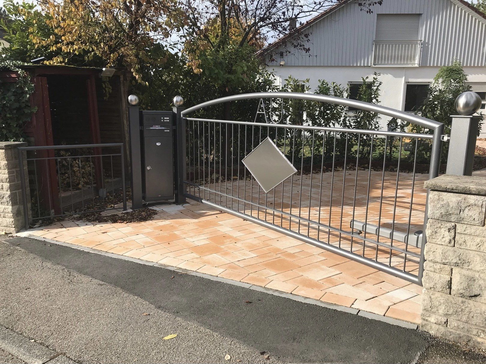 Vor einem Haus öffnet sich ein Edelstahltor zu einer Einfahrt.