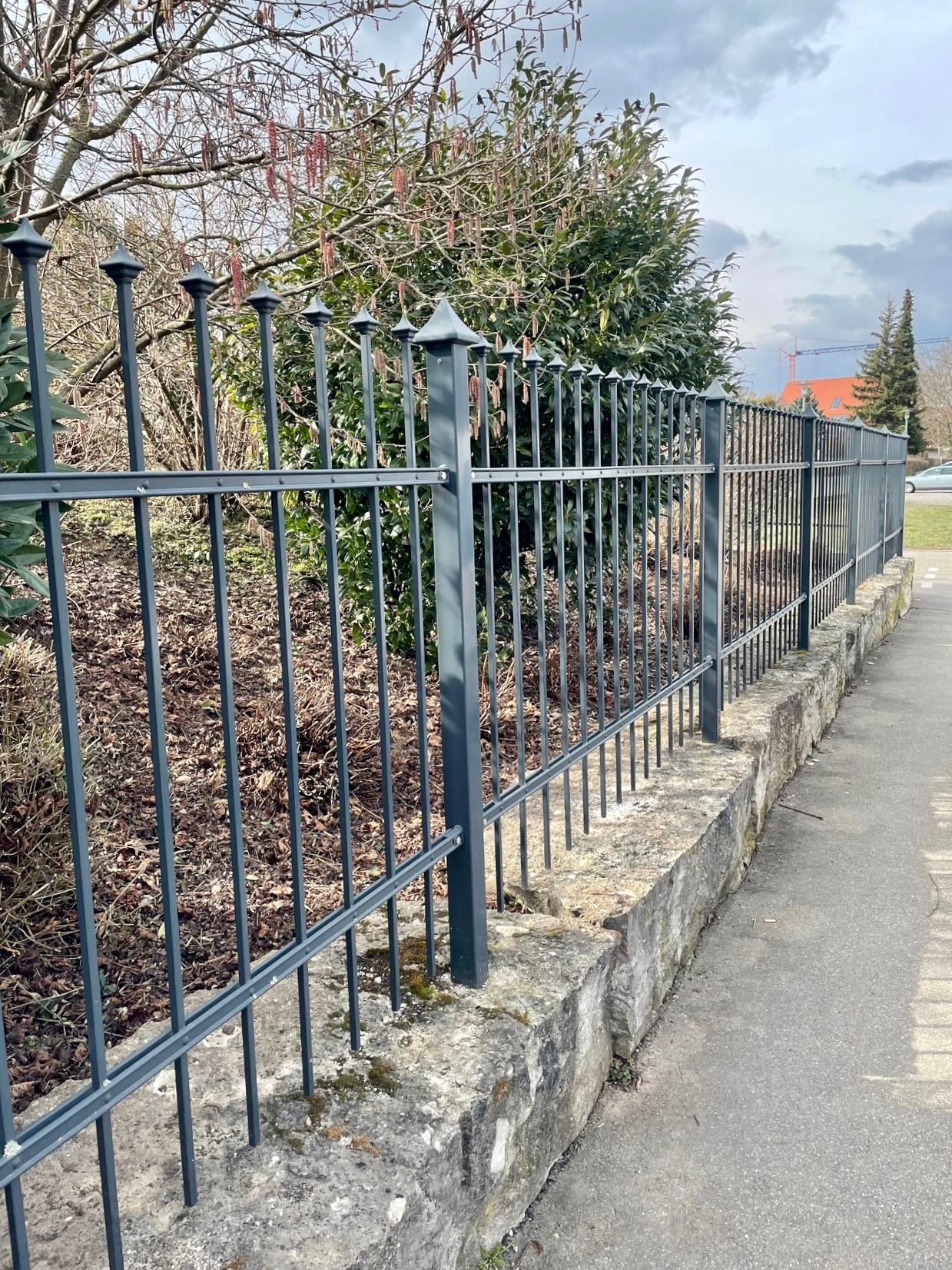 Am Straßenrand steht ein schmiedeeiserner Zaun.