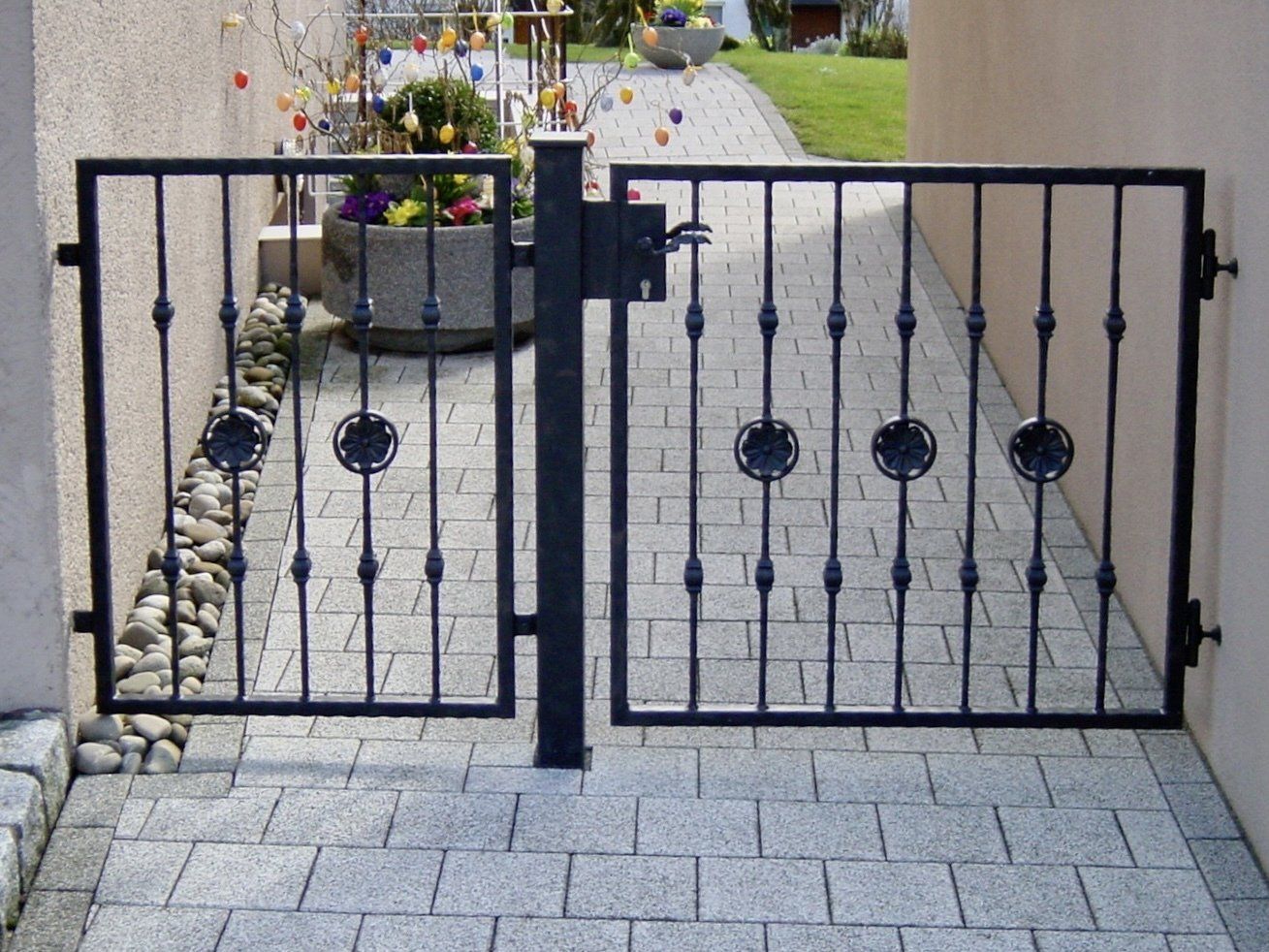 Ein schmiedeeisernes Tor ist zu einem gemauerten Gehweg hin geöffnet