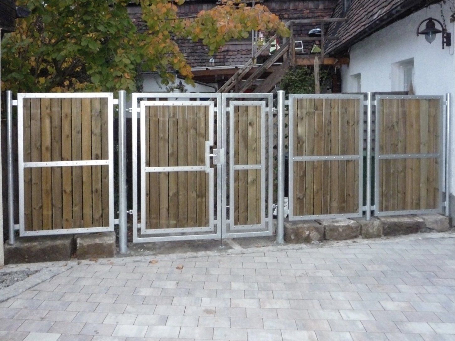 Ein Holzzaun mit Metallrahmen umgibt eine gemauerte Auffahrt