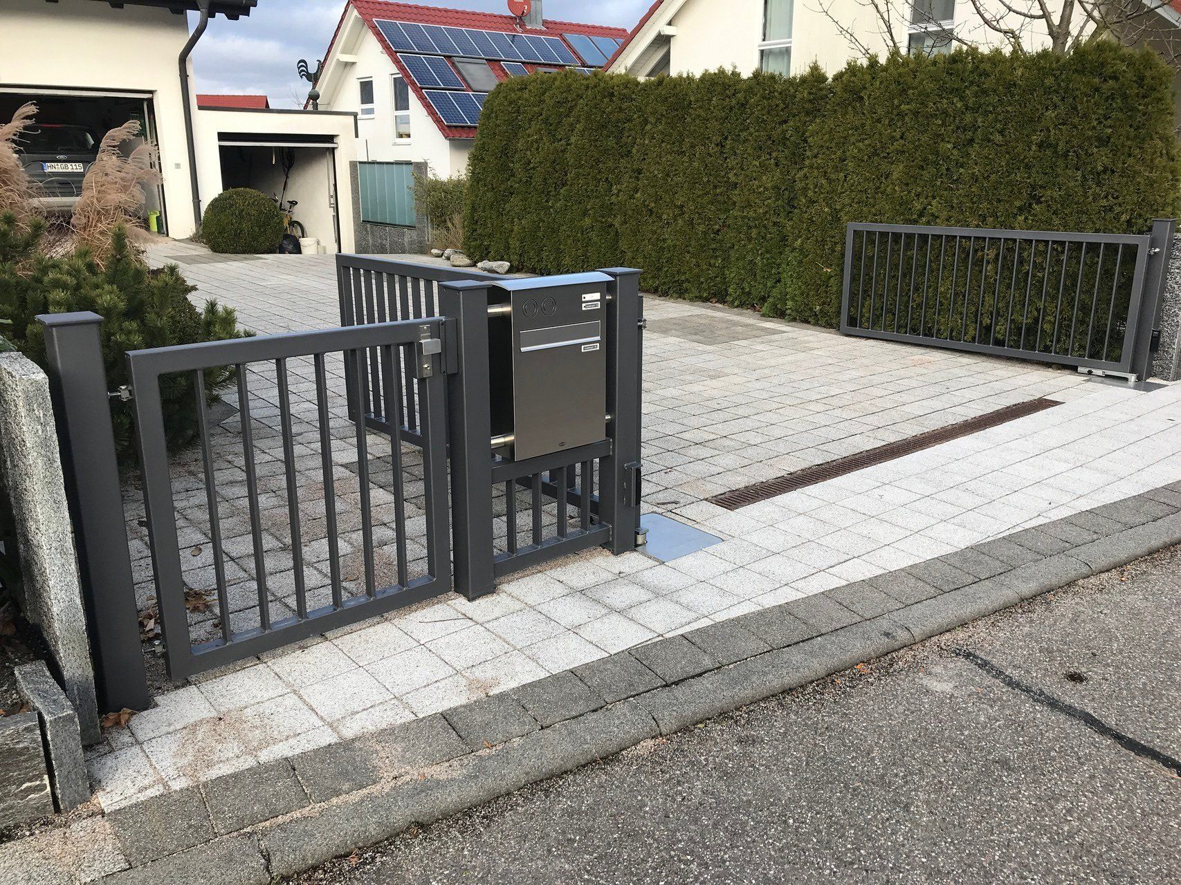 Ein schwarzes Tor mit einem Briefkasten vor einem Haus.