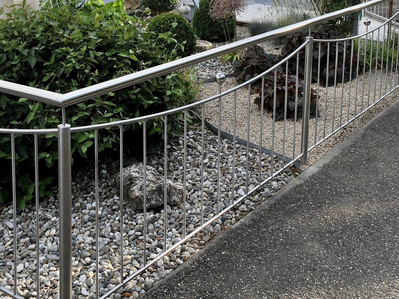 Ein Edelstahlzaun umgibt einen Kiesweg in einem Garten.