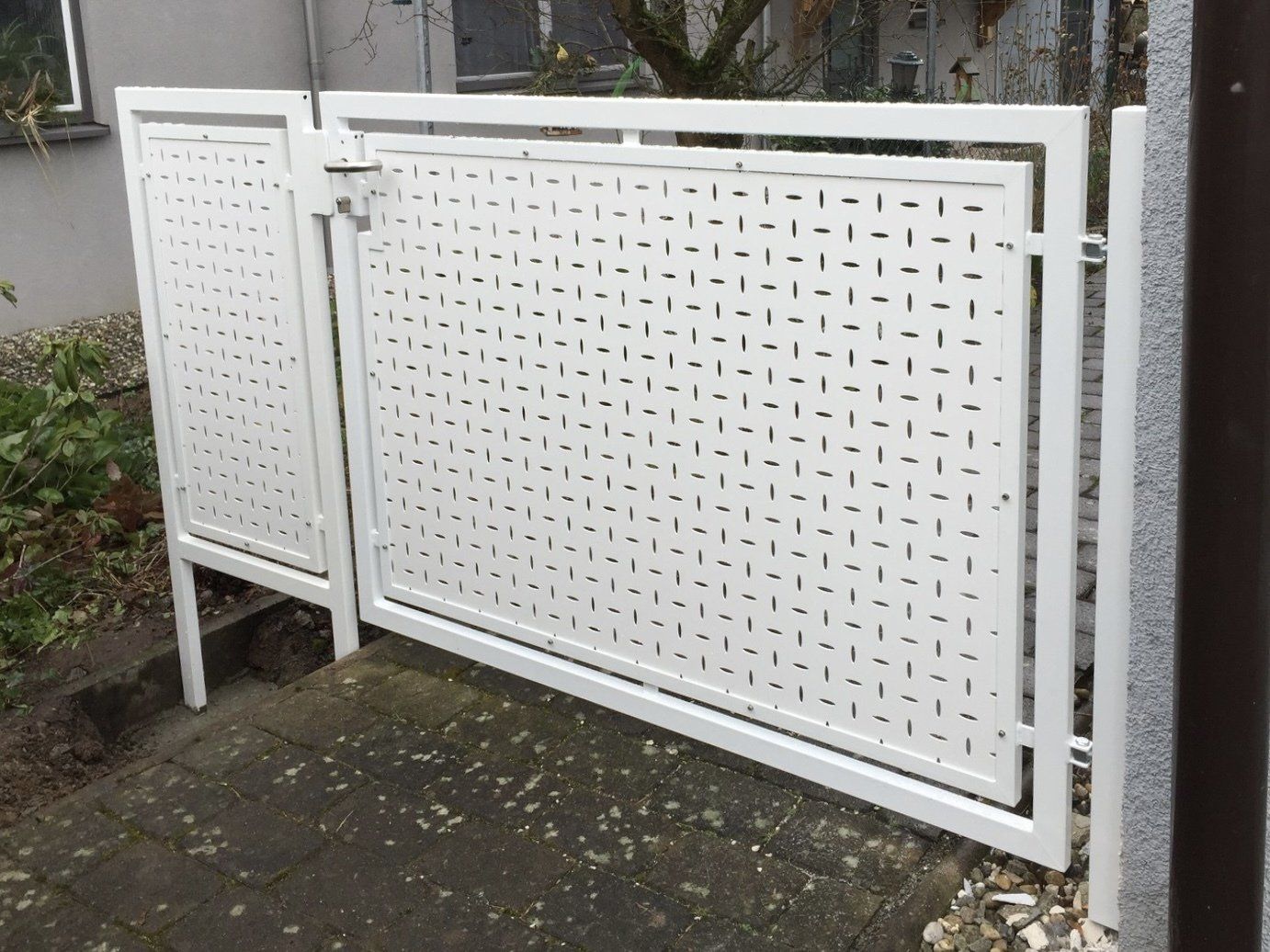 Neben einem Gebäude steht ein weißer Zaun mit Löchern.
