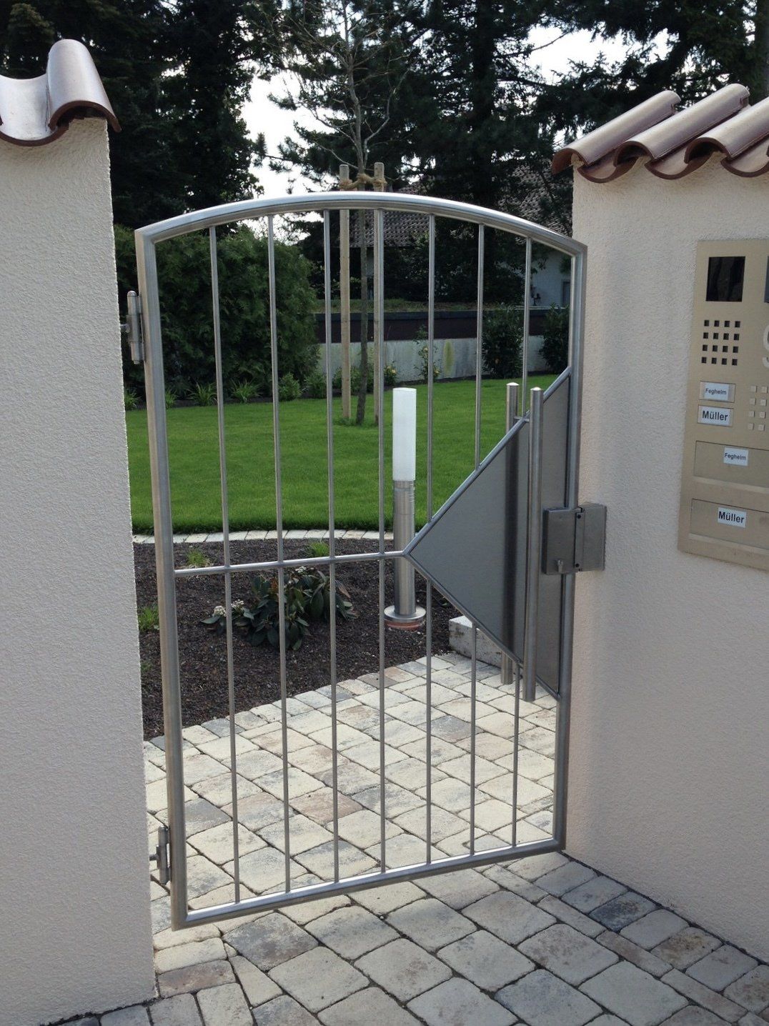 Ein Edelstahltor ist zu einem gemauerten Gehweg hin geöffnet