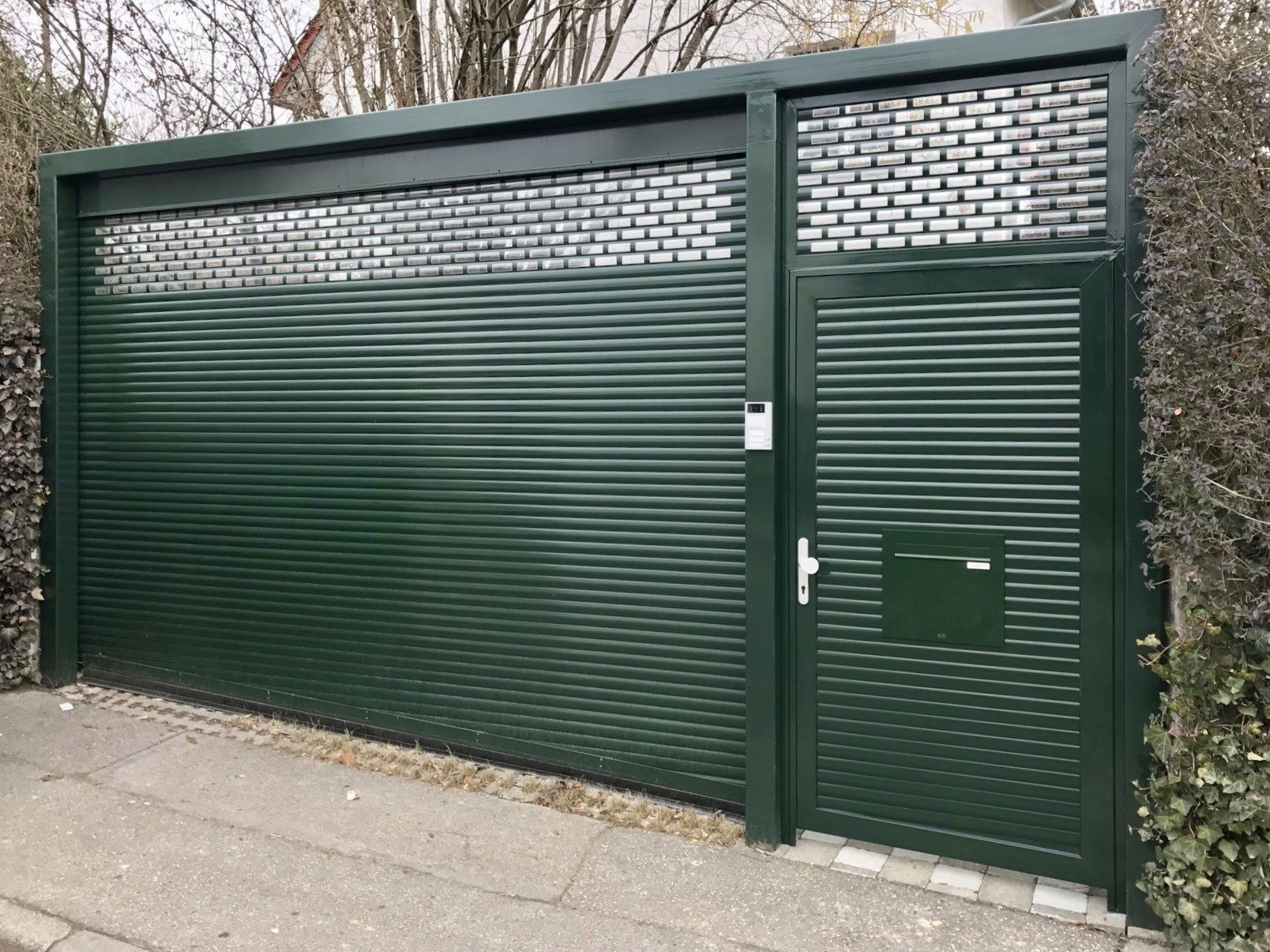 Ein grünes Garagentor mit einem Briefkasten an der Seite.
