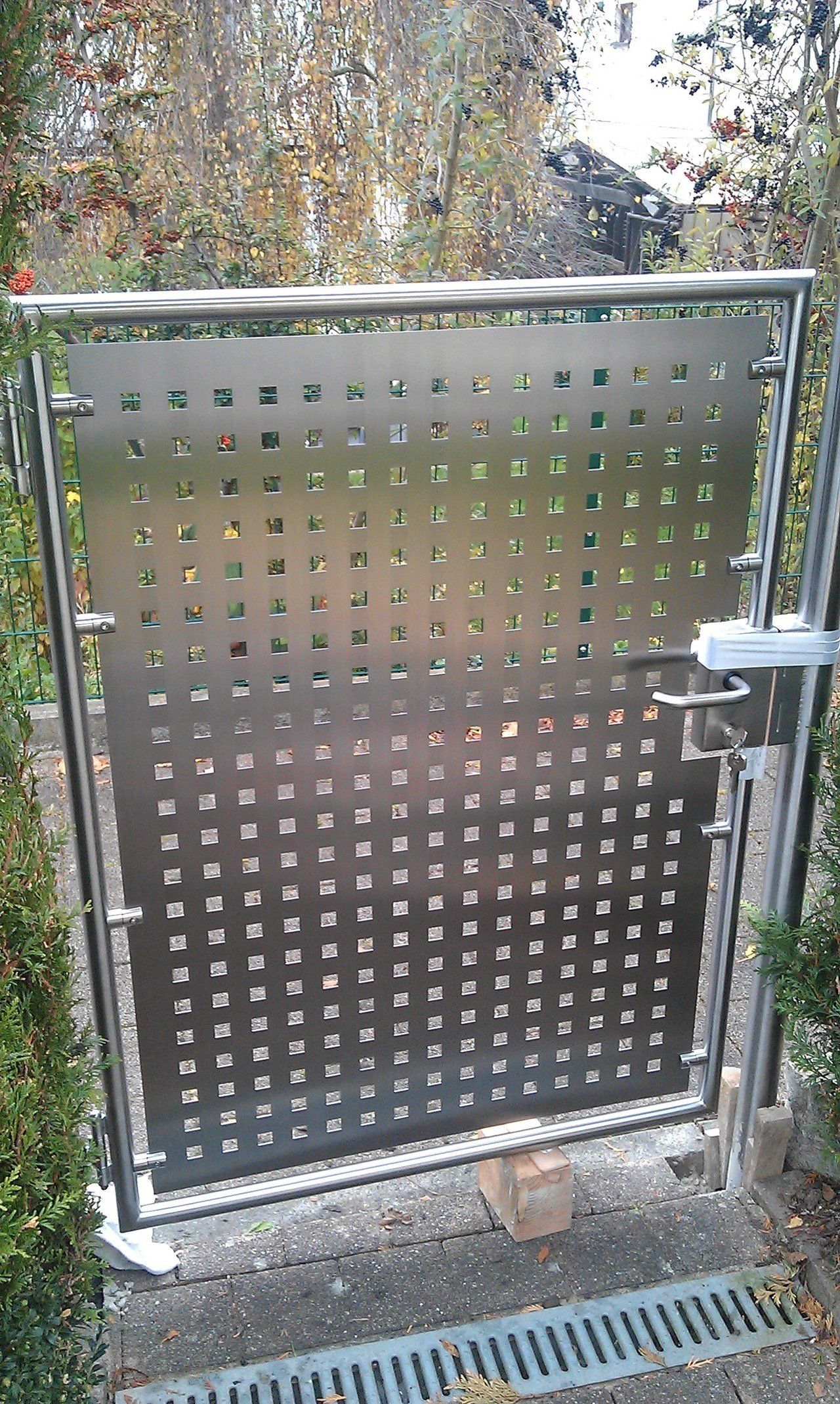 Neben einem Abfluss befindet sich ein Edelstahltor mit Löchern.