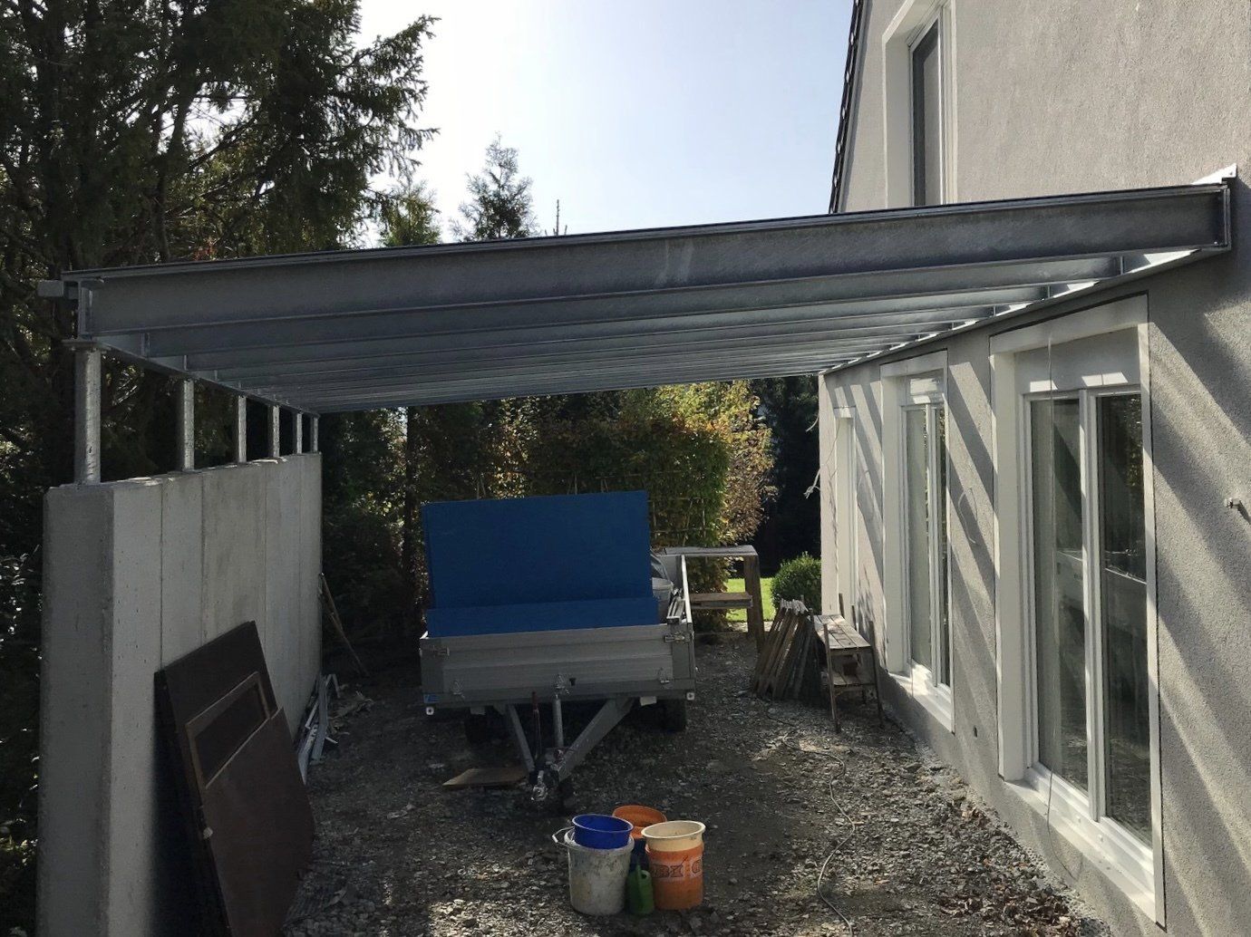 Ein Anhänger ist unter einem Vordach vor einem Haus geparkt.