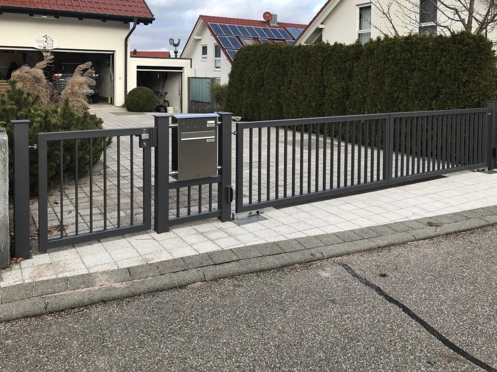 Ein schwarzer Zaun mit einem Briefkasten vor einem Haus