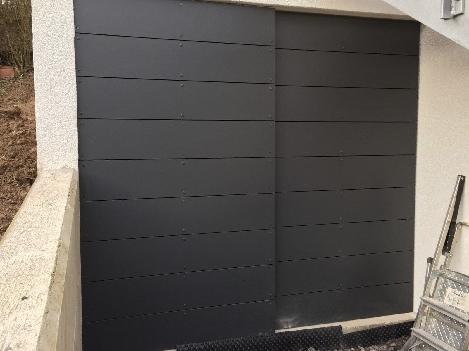 An der Seite eines Gebäudes befindet sich ein schwarzes Garagentor.