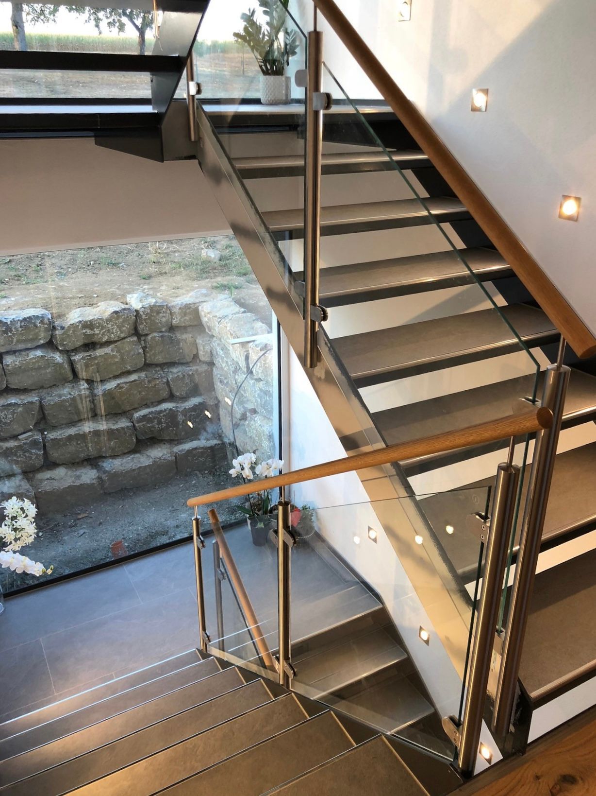 Die Treppe ist aus Edelstahl und Holz gefertigt und verfügt über ein Glasgeländer.