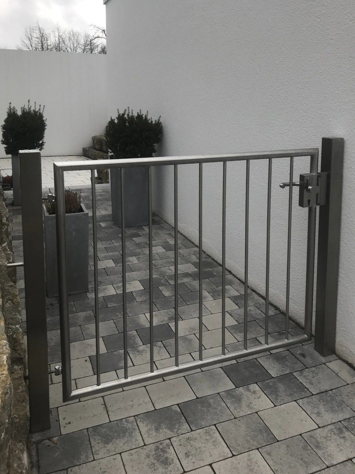Ein Edelstahltor ist zu einem gemauerten Gehweg hin geöffnet.