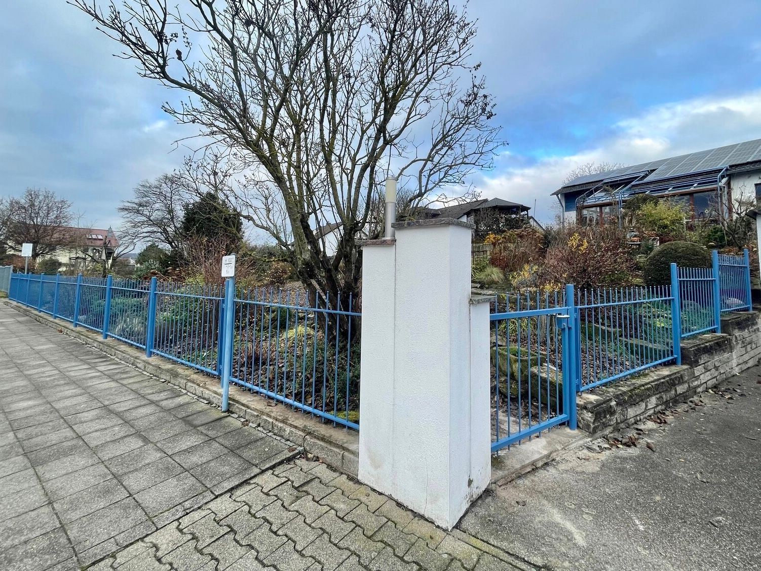 Ein blau-weißer Zaun umgibt einen gemauerten Gehweg.