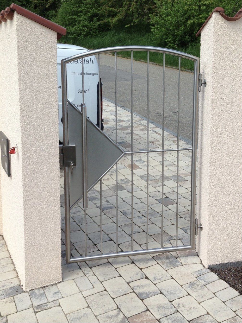 Ein Edelstahltor führt zu einem gemauerten Gehweg.
