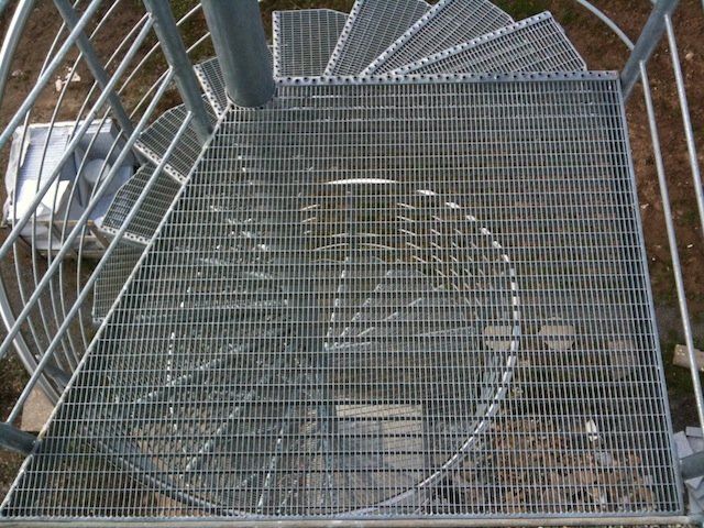 Eine Wendeltreppe aus Metall mit einem im Hintergrund geparkten Auto