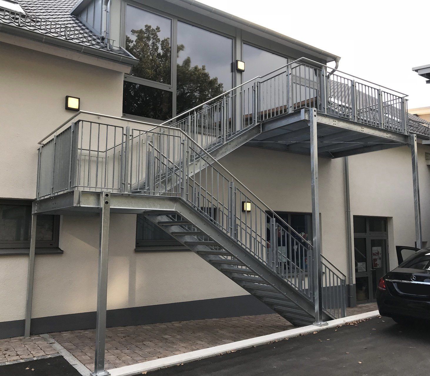 Vor einem Gebäude, zu dem eine Treppe hinaufführt, ist ein Auto geparkt.