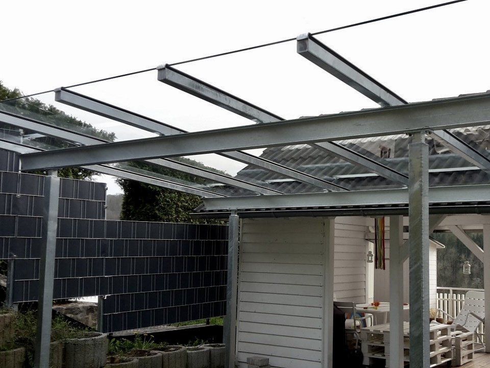 Eine Pergola mit einem klaren Glasdach steht vor einem Haus