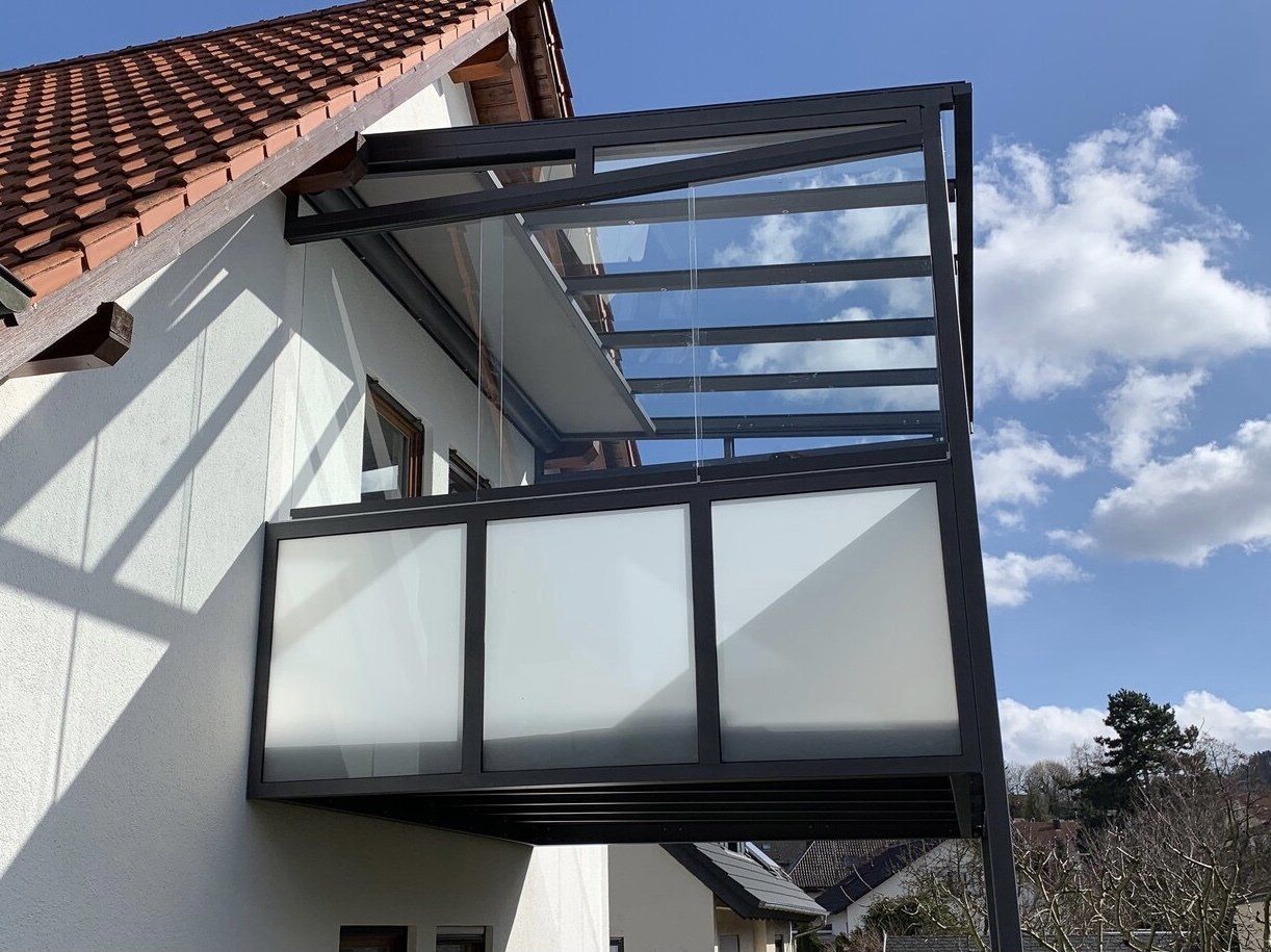 An der Seite eines Hauses befindet sich ein Balkon mit Glasdach.