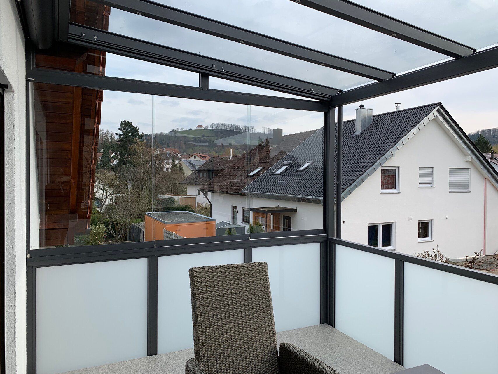 Ein Balkon mit Stuhl und Tisch und Blick auf ein Haus.