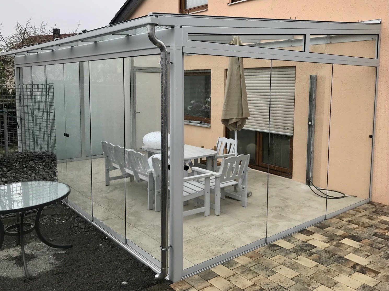 Eine Terrasse mit Tisch und Stühlen unter einem Glasdach.