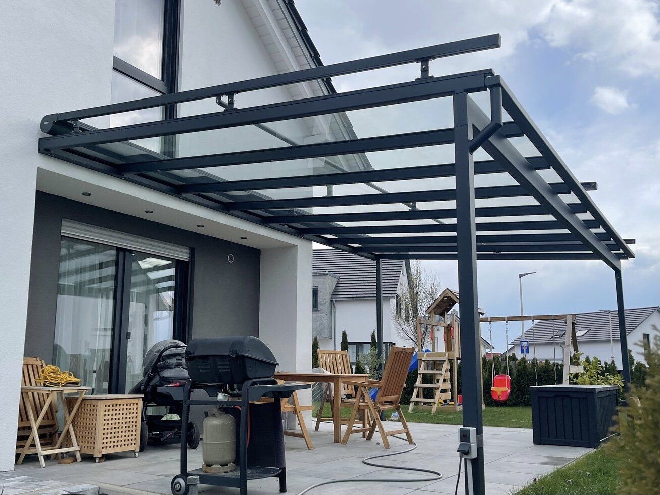 Eine Terrasse mit Grill, Tisch und Stühlen unter einem Baldachin.