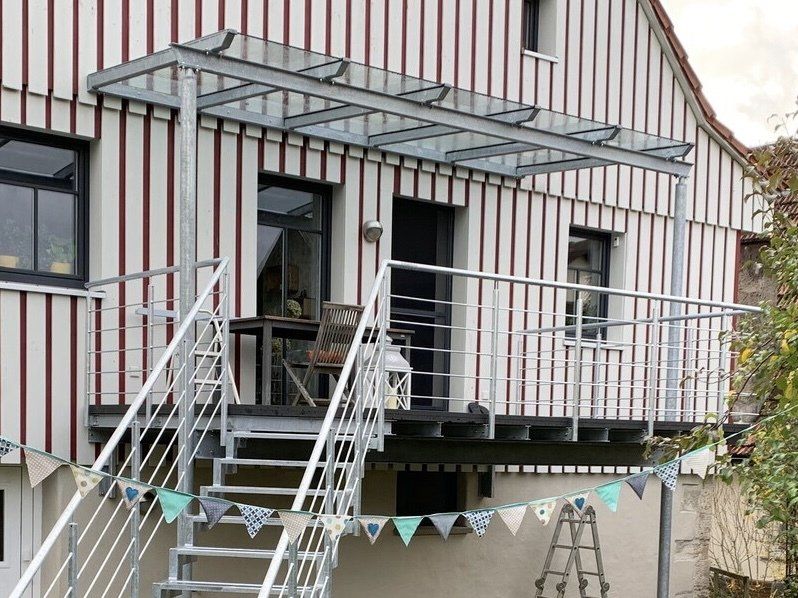 Ein Haus mit einer Treppe, die zu einem Balkon mit Glasdach führt.