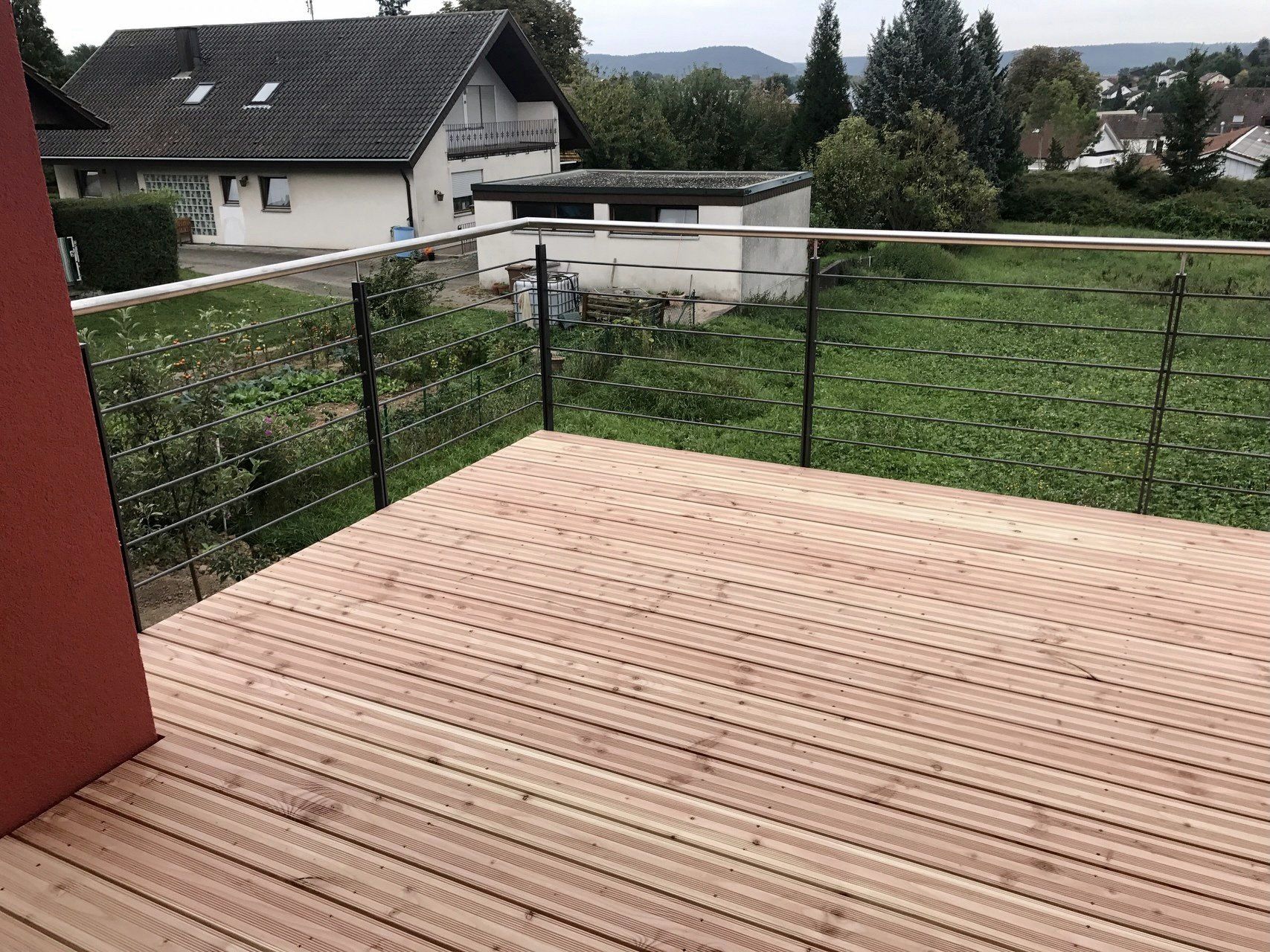 Ein Holzdeck mit Edelstahlgeländer und Blick auf ein Haus.