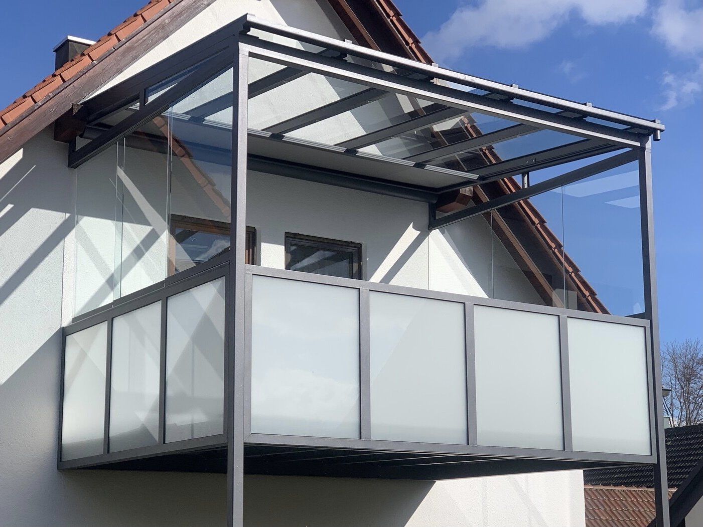 An der Seite eines Hauses befindet sich ein Balkon mit Glasdach.