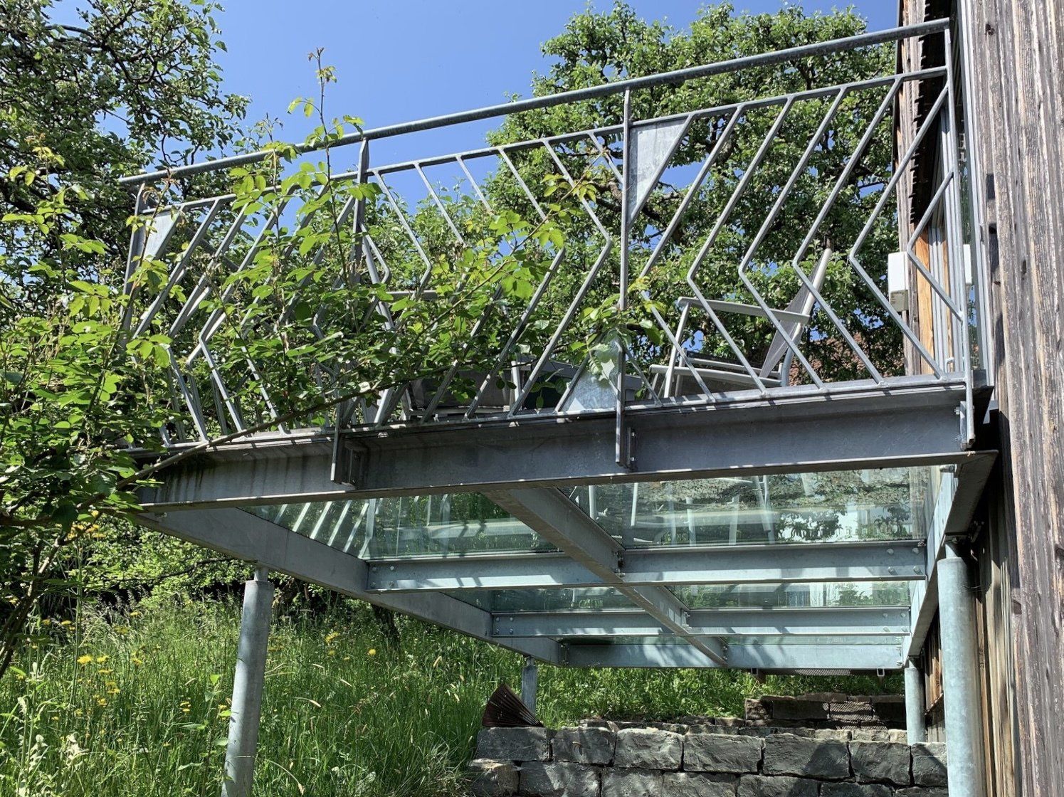 Ein Balkon mit einem Geländer aus Edelstahl ist von Bäumen umgeben.