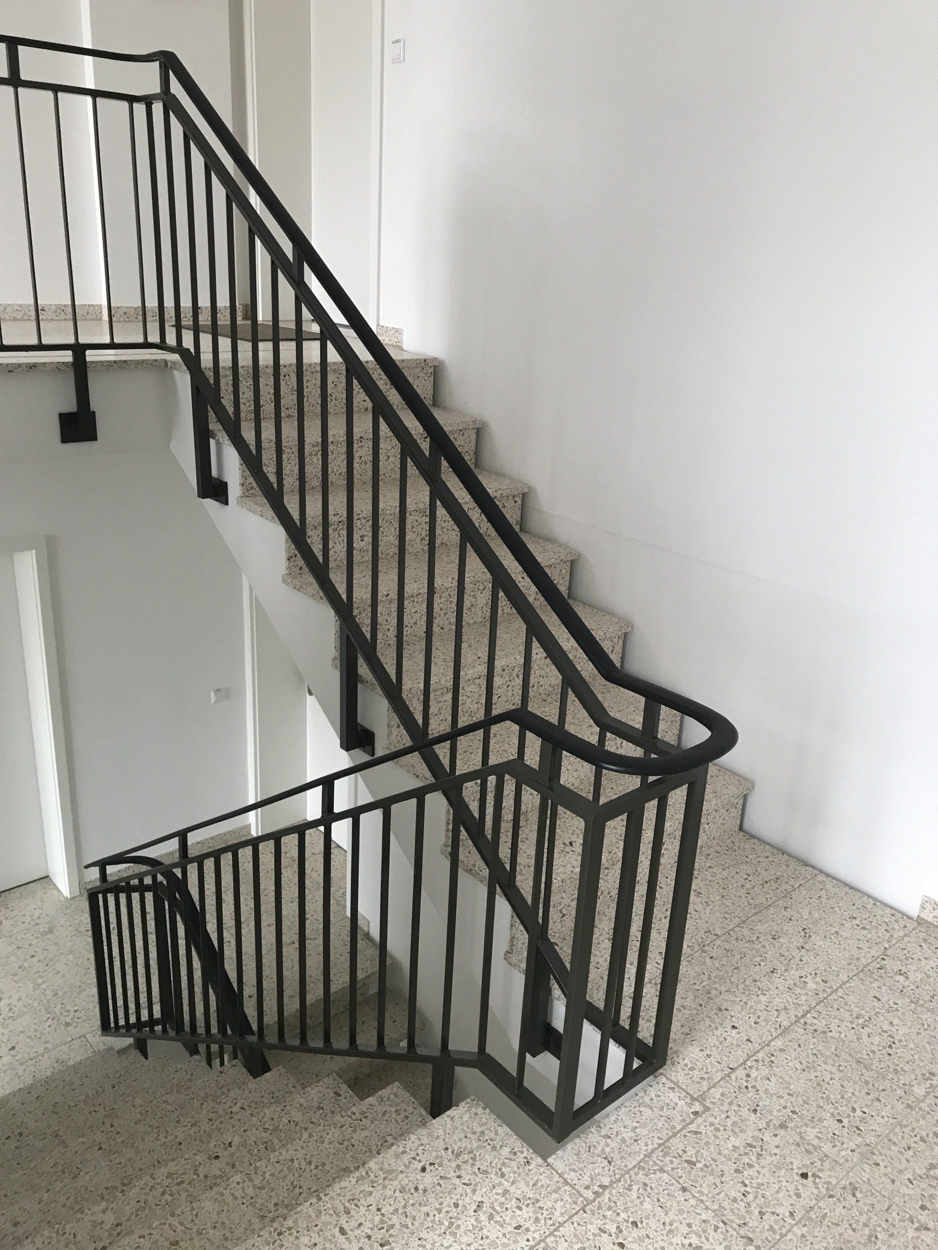 Eine Treppe mit schwarzem Geländer und weißer Wand