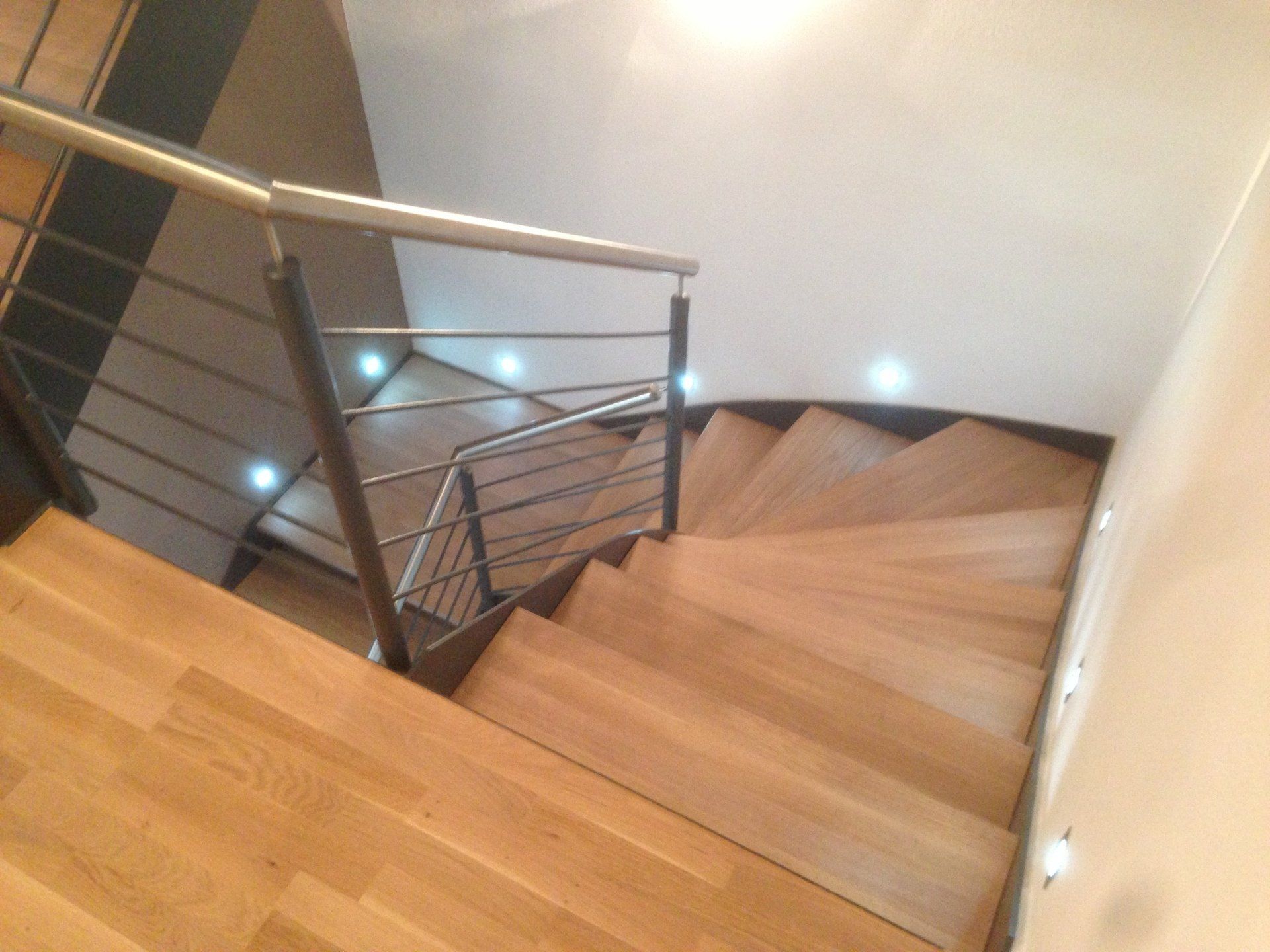 Eine Holztreppe mit einem Metallgeländer und Lichtern auf den Stufen