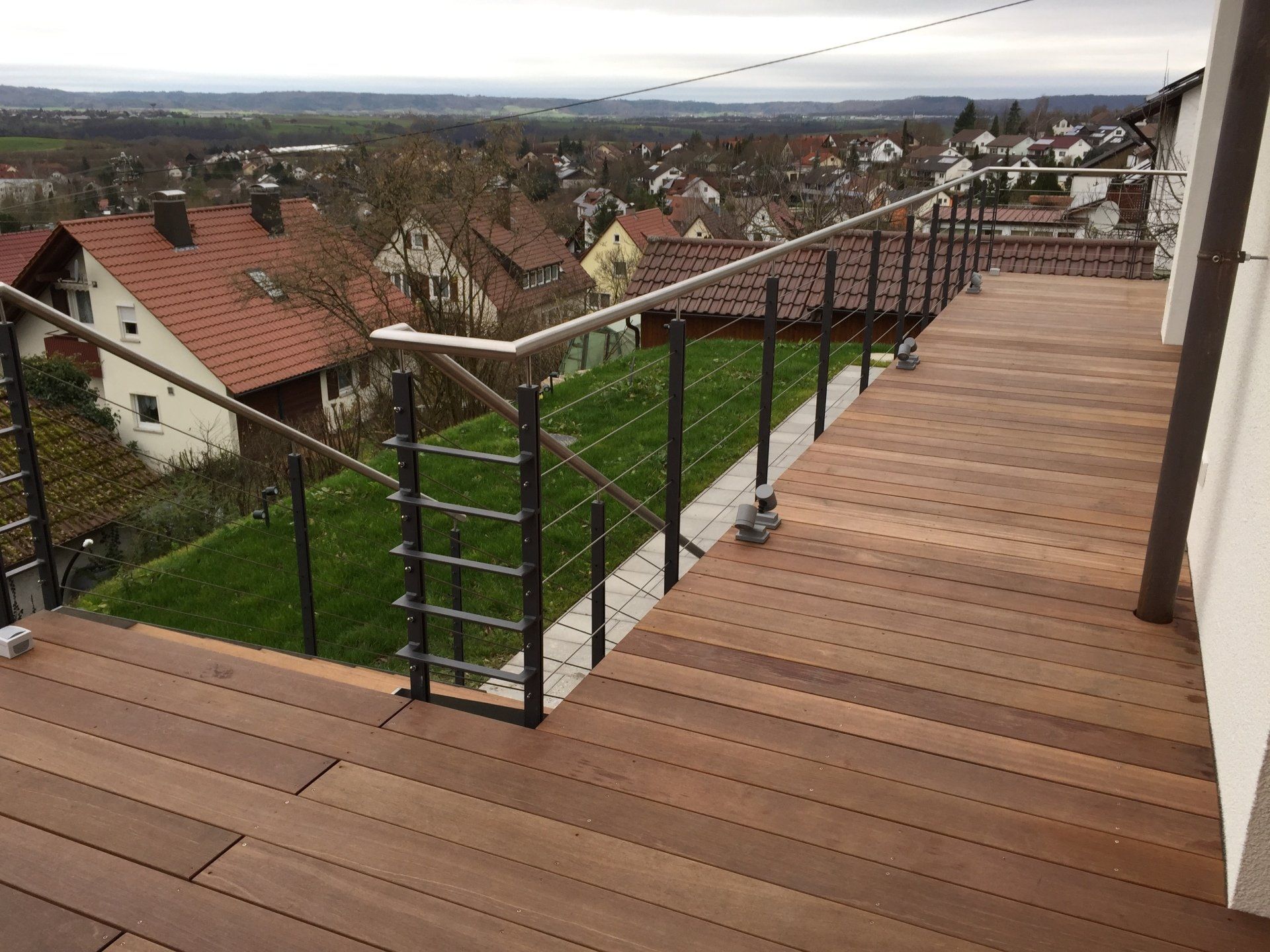 Ein Holzdeck mit einem Geländer aus Edelstahl und einer Treppe, die dorthin führt.