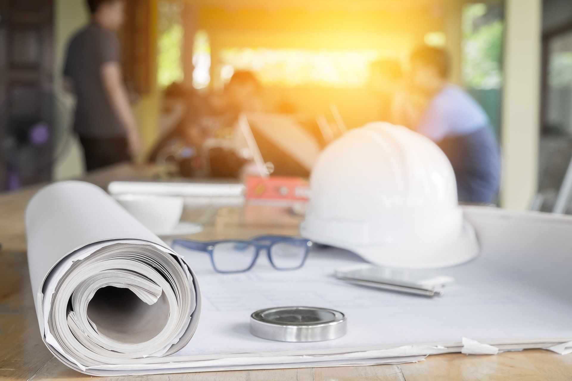 Eine Rolle Blaupausen, ein Schutzhelm, eine Brille und Klebeband auf einem Tisch.