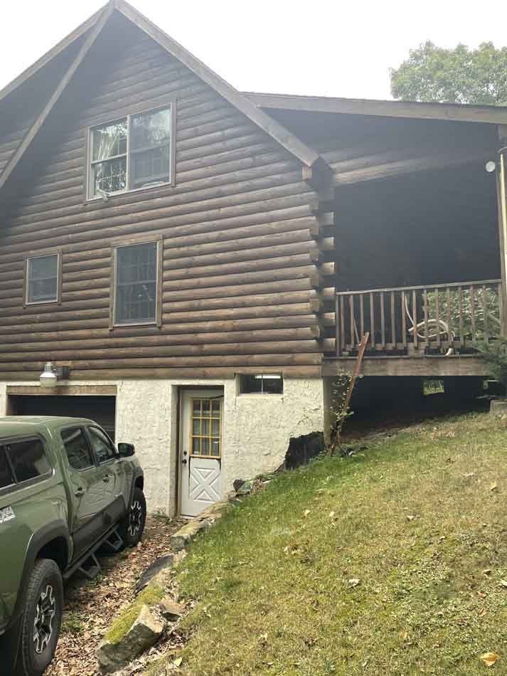 Log cabin with a truck parked beside a lower level with a small door.