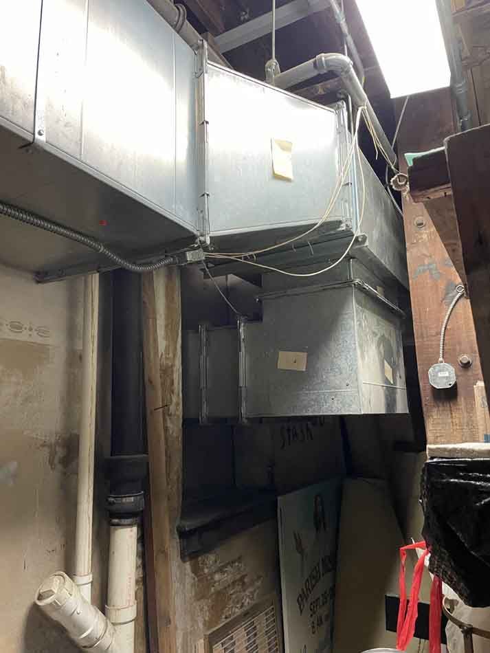 Metallic HVAC ductwork in a basement, with electrical wiring and pipes.