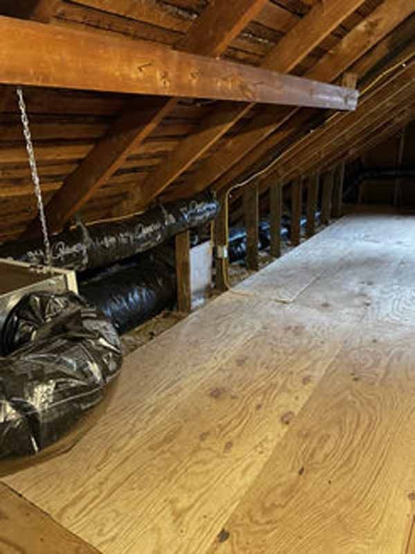 Attic with plywood flooring, ductwork, exposed beams and rafters.