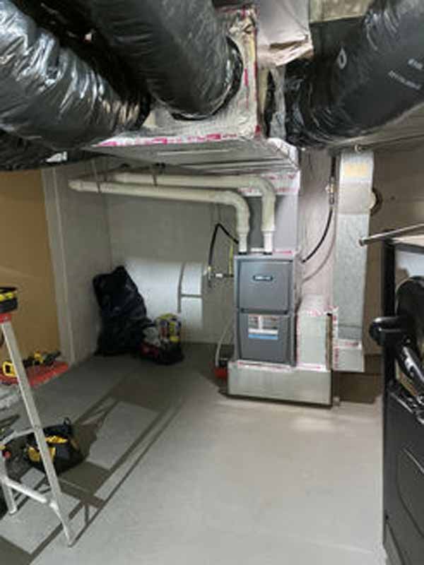 HVAC system in a basement, with ductwork and furnace. White pipes, black ducts, gray walls.