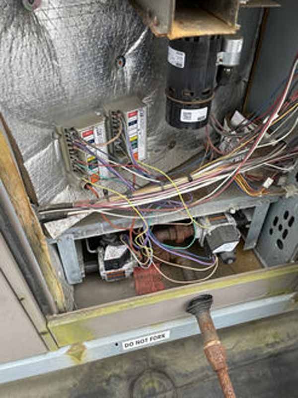 Furnace interior showing wires, electrical components, and gas valves, in a metallic enclosure.