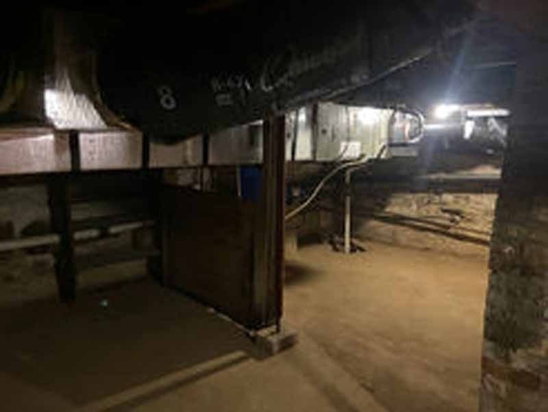 Dark basement with beams, pipes, and exposed brick.