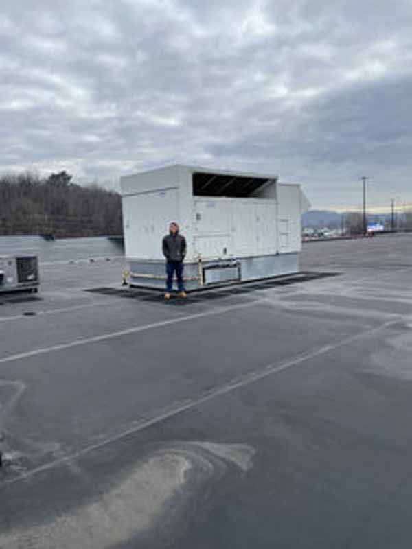 Man standing in front of a large white HVAC unit on a rooftop, overcast sky in the background.