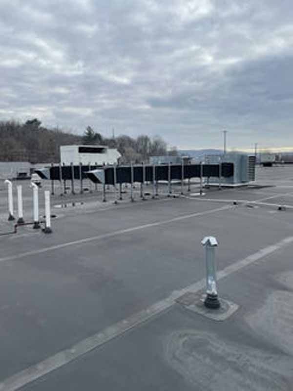 Rooftop with HVAC equipment. Gray flat roof, white pipes, industrial setting under cloudy sky.