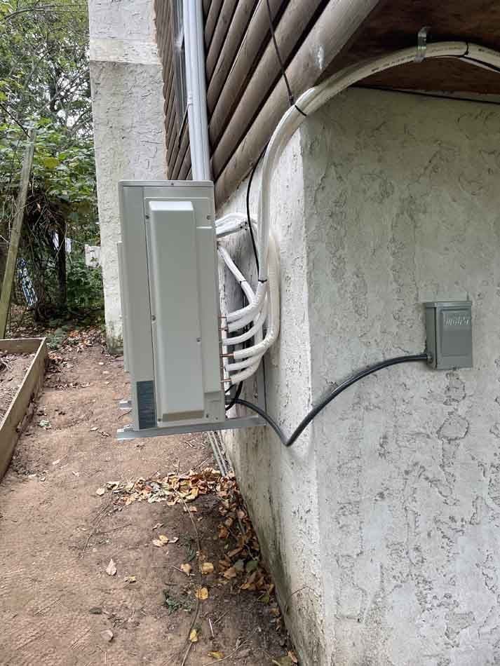 Outdoor AC unit mounted on stucco wall next to electrical outlet and conduit pipes.