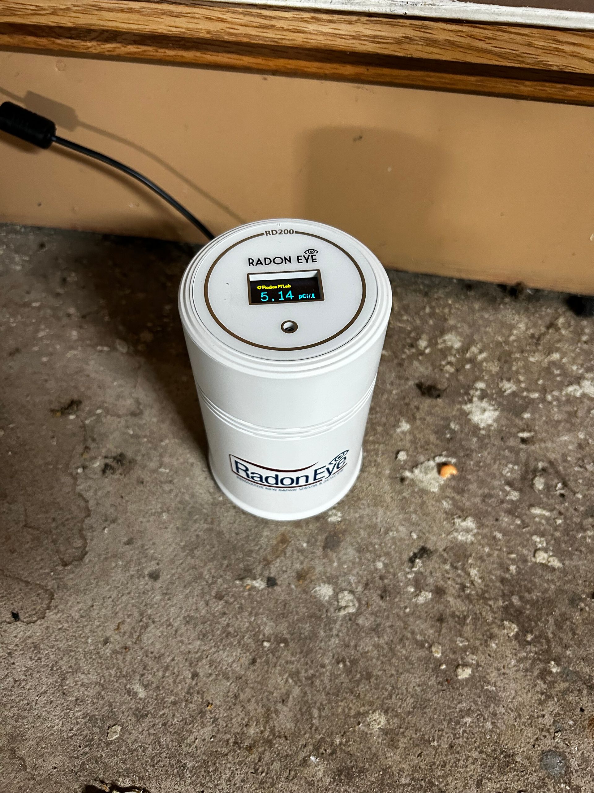 White cylindrical air quality monitor on concrete floor. A cord extends from the top.