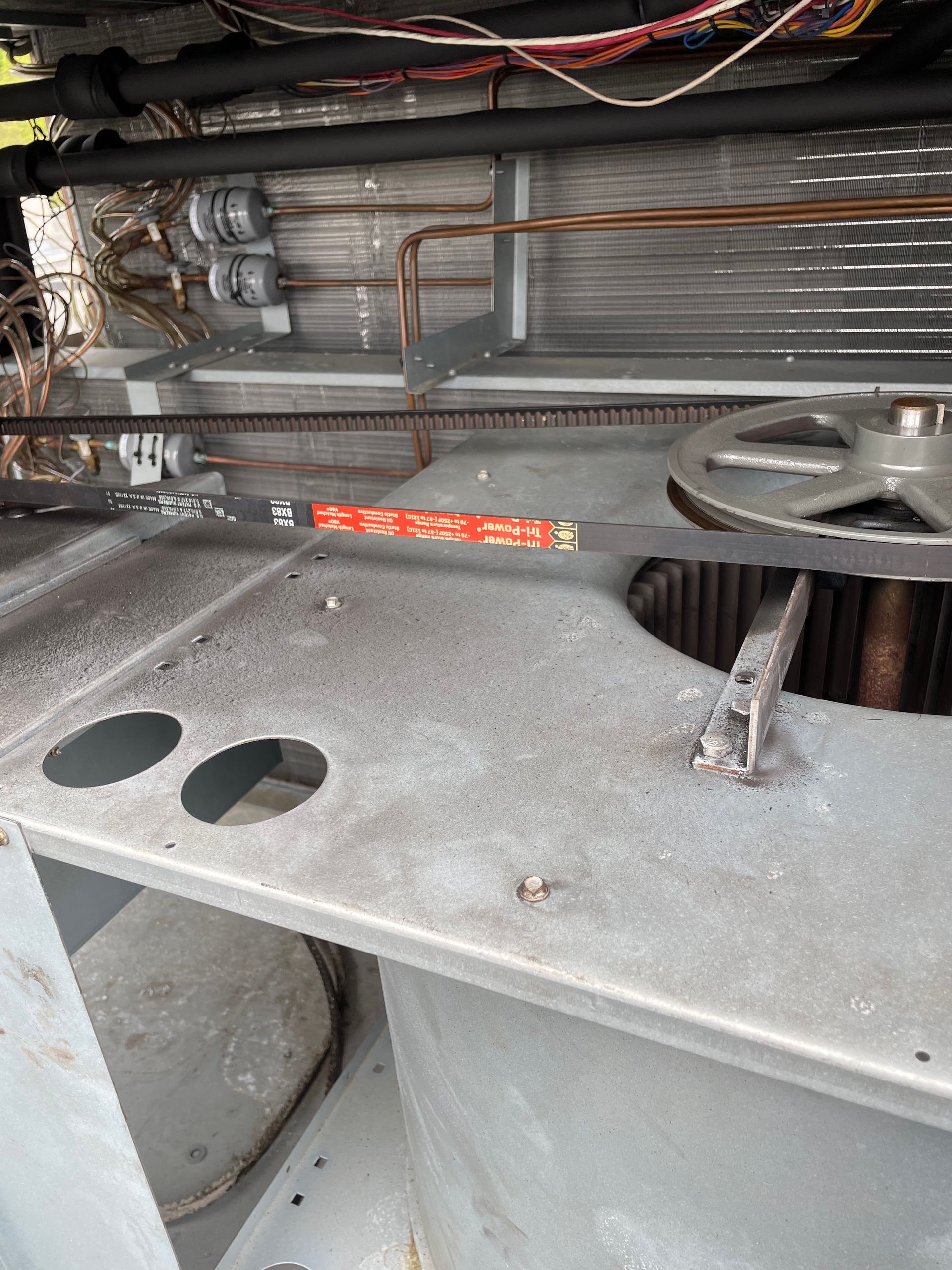 An HVAC unit, showing a belt, pulleys, and copper tubing. Gray metal with various wires.