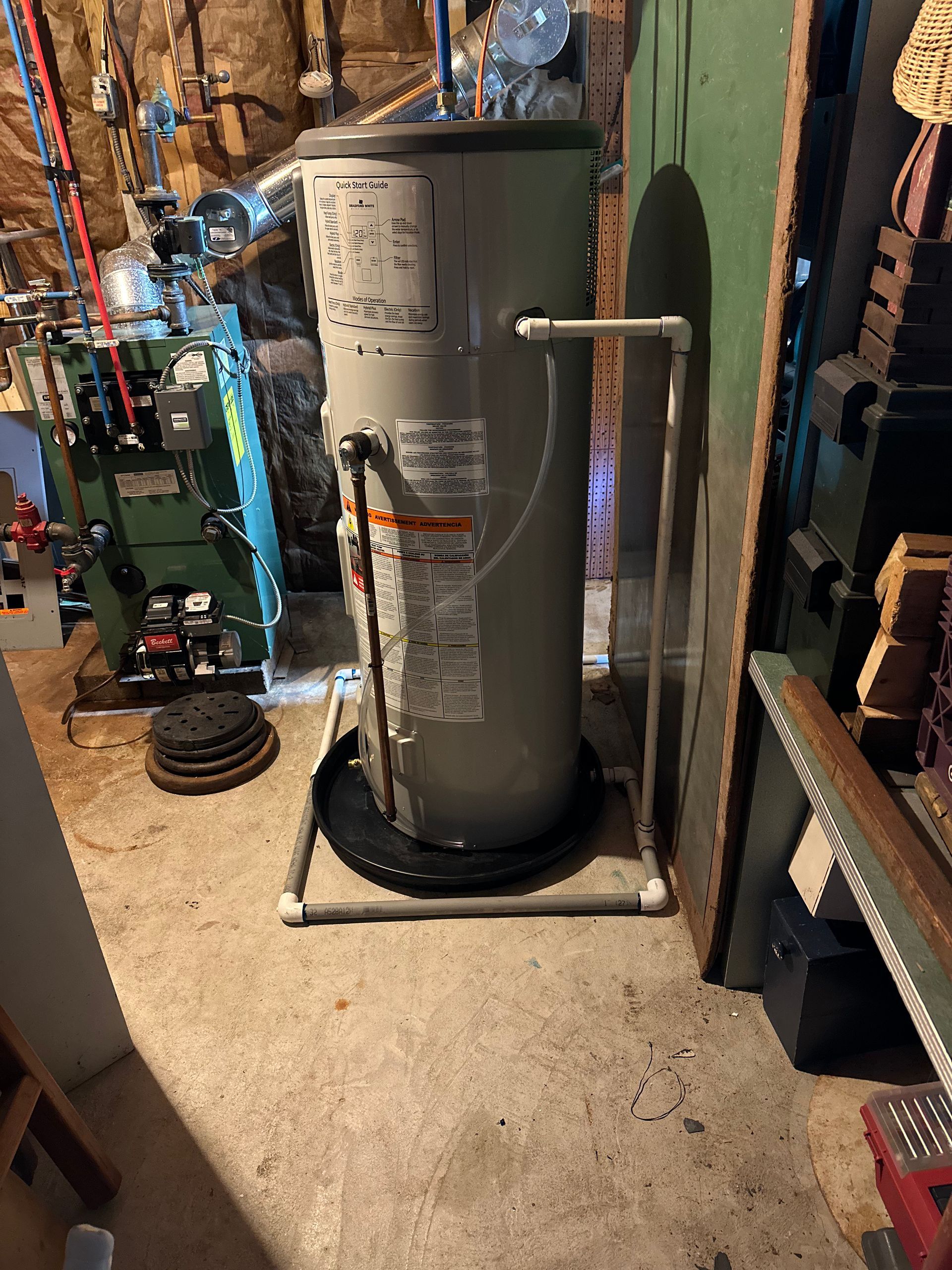 Water heater in a basement, with a PVC pipe stand and other plumbing visible.