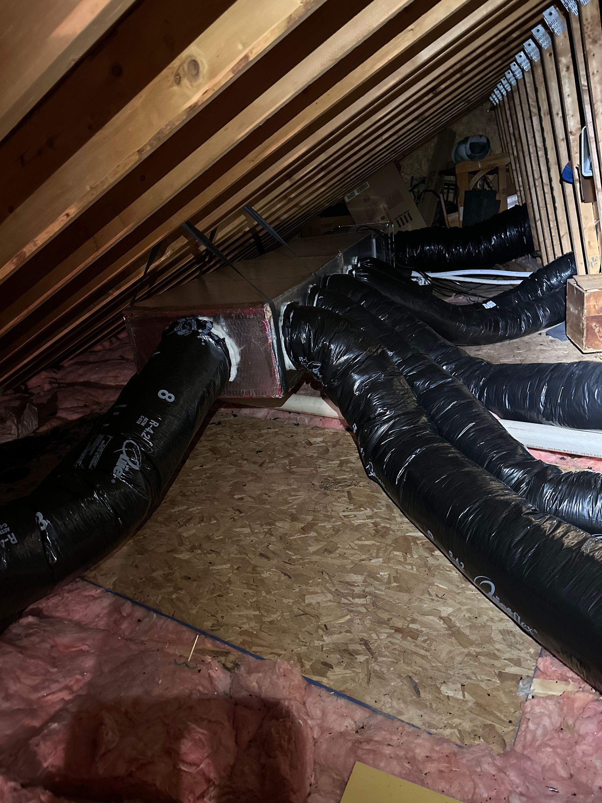 Attic view with ductwork connected to a central box. Black flexible tubes run from the box among wooden rafters.
