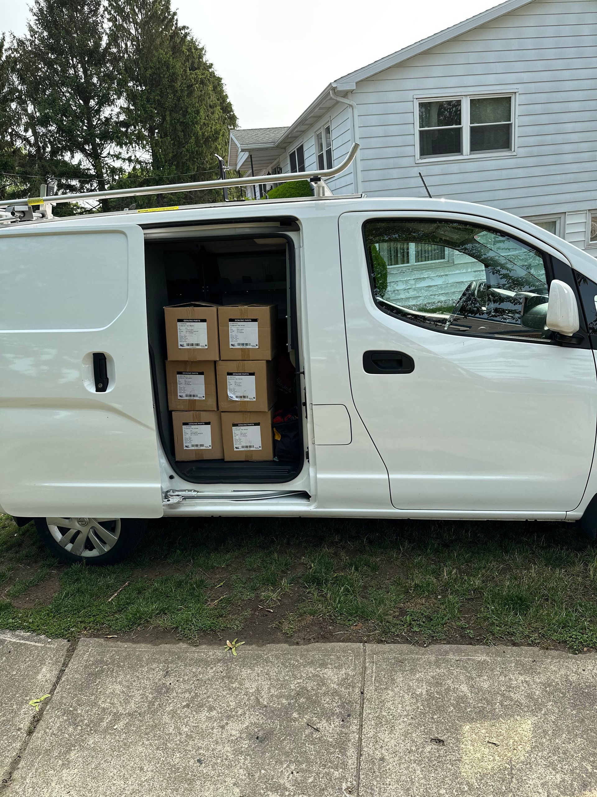 White cargo van with open side door, boxes inside, parked on grass near a house.