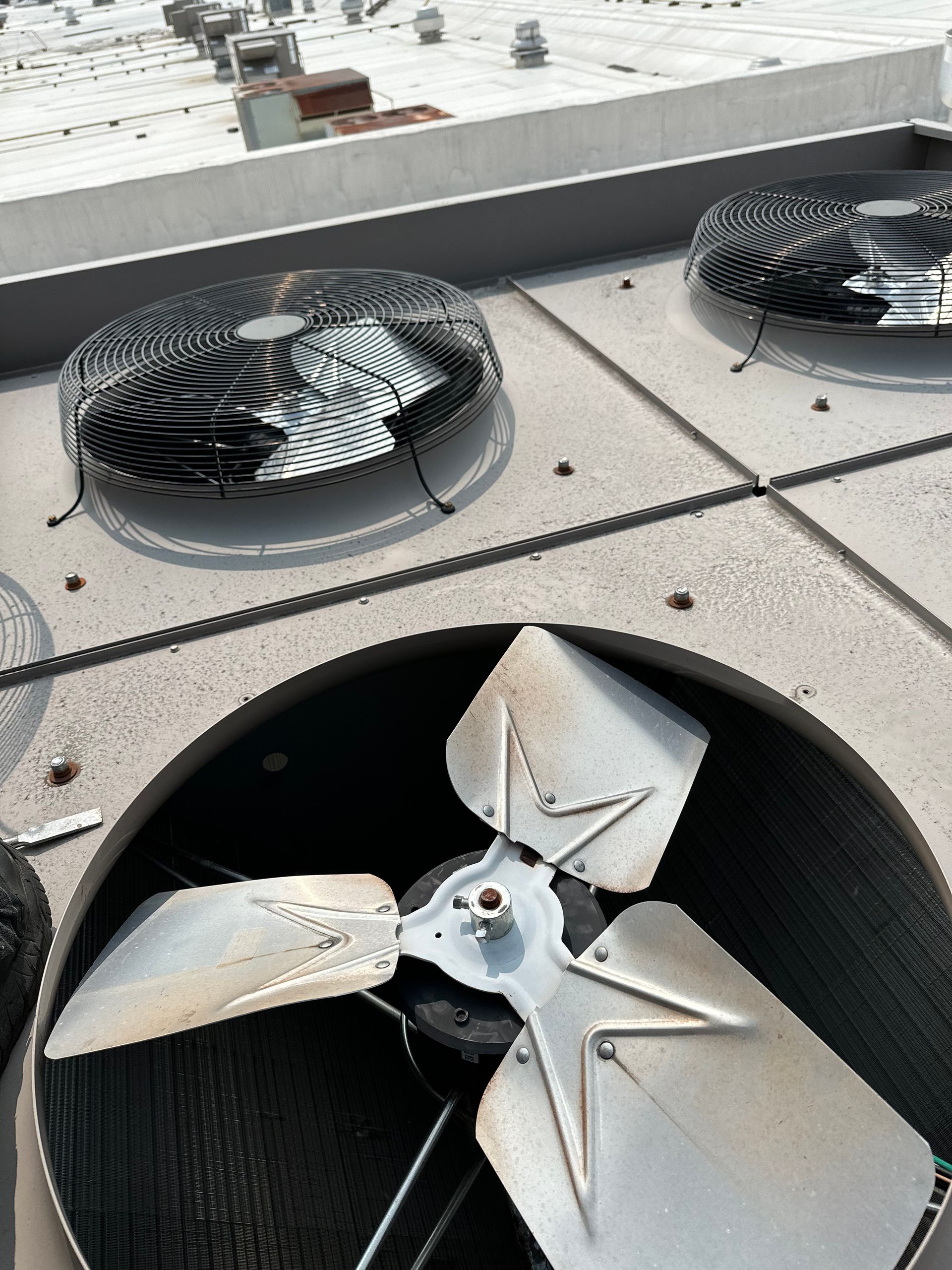 A close-up of a rooftop HVAC unit with a fan and protective grill.